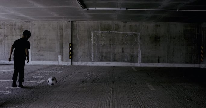 HANDHELD Teenager kid boy soccer player practicing kicks and moves inside empty covered parking garage. 4K UHD 60 FPS RAW graded footage