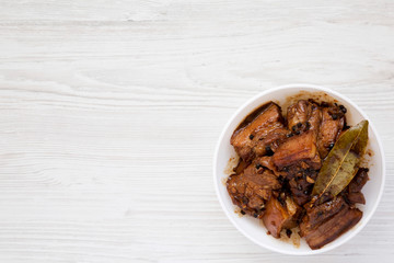Homemade Filipino Adobo Pork in a white bowl, overhead view. Flat lay, from above, top view. Copy space.