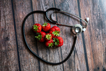 Stethoscope with strawberries on top of wooden table. Medical and healthcare conceptual.