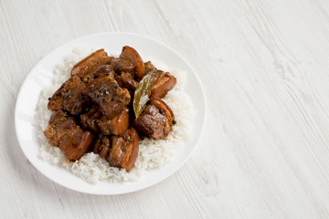 Homemade Filipino Adobo Pork with rice on a white plate over white wooden background, low angle view. Copy space.