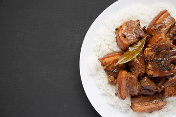 Homemade Filipino Adobo Pork with rice on a white plate over black surface, top view. Flat lay, overhead, from above. Copy space.