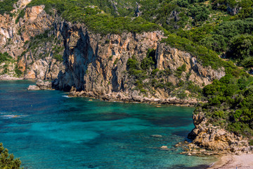 Beautiful landscape with sea–lagoon with turquoise water, mountains and cliffs, green trees, blooming bushes and flowers, rocks in a blue water. Corfu Island, Greece. 