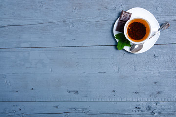 White cup of mint tea with lemon and chocolate on a blue gray wooden background, top view, empty space