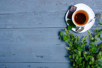 White cup of mint tea with lemon and chocolate on a blue gray wooden background, top view, empty space