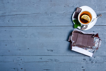 White cup of mint tea with lemon and chocolate on a blue gray wooden background, top view, empty space
