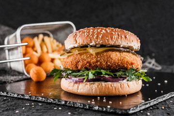 Chicken burger with pickles, arugula, sauce and fried stick balls, french fries on slate black...