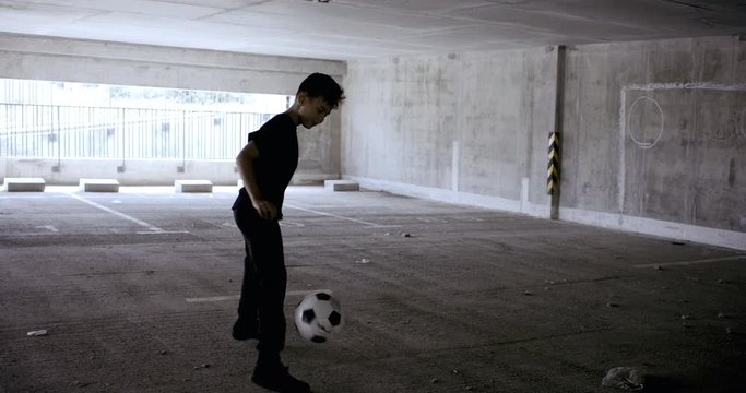 HANDHELD Teenager kid boy soccer player practicing kicks and moves inside empty covered parking garage. 4K UHD 60 FPS RAW graded footage