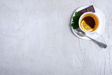 White cup of mint tea with lemon and chocolate on gray white stone table background, top view, empty space