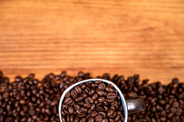 Coffee beans over a wooden table top with a coffee mug full of beans.