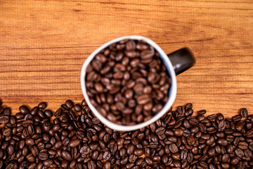 Coffee beans over a wooden table top with a coffee mug full of beans.