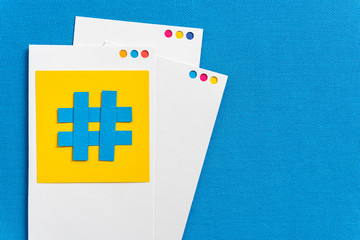 Paper cutout of hashtag symbol with mobile device concept made with paper on a blue textured background. Concept of social media and digital marketing.