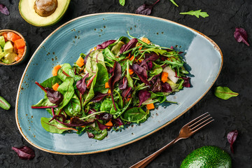 Fresh green salad with mixed greens, spinach arugula, pumpkin, avocado in plate over dark background. Healthy food, clean eating, vegan dieting, top view
