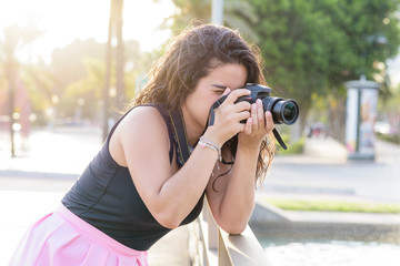 Portrait of young woman  making photos with a professional digital camera in a city.