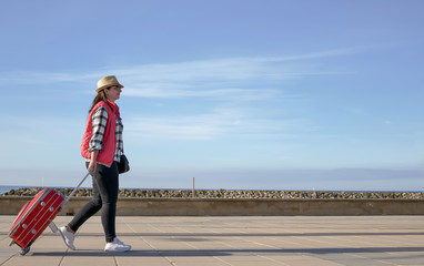 Attractive young woman tourist with a red suitcase is walking alone along the street, copyspace