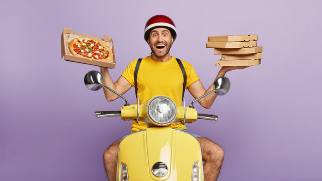 Friendly looking delighted delivery man holds cardboard boxes, one opened container with delicious pizza, transports food items from cafe to clients, brings orders by motorbike, likes his job