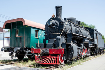 A black Soviet steam locomotive with a star and an old passenger green wooden carriage stand nearby...