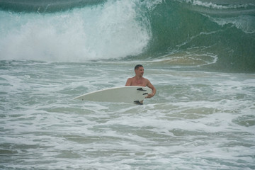 Young man with surfboard running in the ocean in the rain