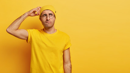 Clueless man scratches head with questioned doubtful expression, cannot understand friends hint,...