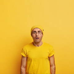 Intense stupefied man stares at camera with bugged eyes, cannot believe in bad news, realizes he made huge mistake, stunned by something, wears bright yellow hat and casual t shirt. Omg concept