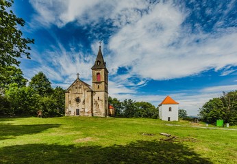 Fototapeta na wymiar Krasikov, Kokasice / Czech Republic - August 9 2019: View of the church of Mary Magdalene and a bell tower. Sunny summer day. Green grass, blue sky with white clouds.