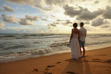 Young couple in love on a romantic date meets the sunset on the beach, holding hands. Rear view