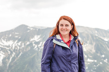 Young woman with backpack standing on cliff's edge. Trekking and tourism concept. Copyspace A young pretty redheaded woman standing on a background of mountains