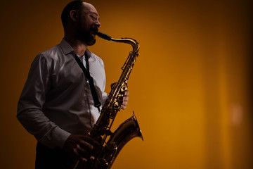 Fototapeta na wymiar Portrait of professional musician saxophonist man in white shirt plays jazz music on saxophone, yellow background in a photo studio, side view