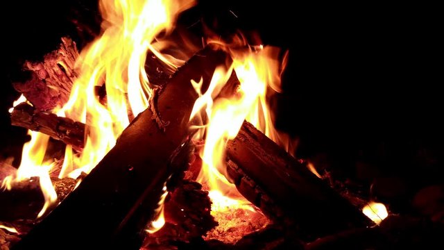 Slow rising view of logs on a campfire with yellow flames roaring out