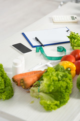 clipboard with pen, measure tape, smartphone with blank screen, calculator, medicine and fresh vegetables on table