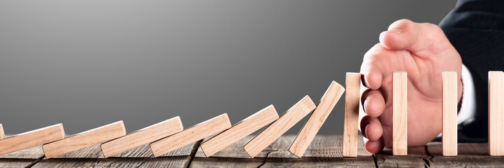 Hand of businessman Blocking Domino Effect On Wooden Table - Investment Protection And Security...