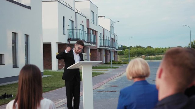 Attractive funny auctioneer leading a property auction sale pointing on people bids banging a gavel at tribune. Successful real estate shopping.