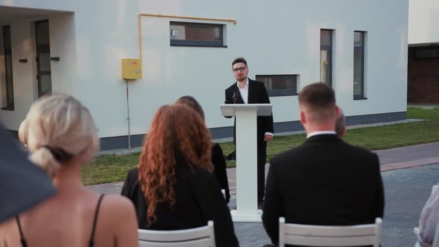 House auction sale. Excited audience of formal people raising hands bidding for real estate property. Attractive auctioneer waving with mallet gavel leading an event.
