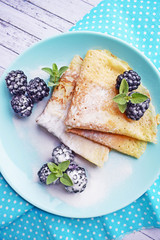 Delicious hot pancakes with blackberries and mint on a wooden background.