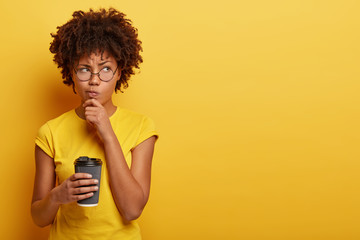 Pensive displeased woman with dark skin, holds chin and looks away, contemplates about something,...