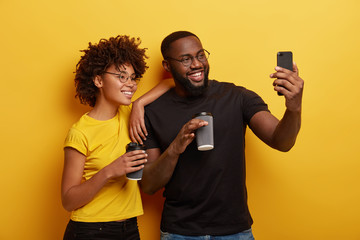 Happy dark skinned couple in love have fun during coffee break, make selfie portrait on modern cell...