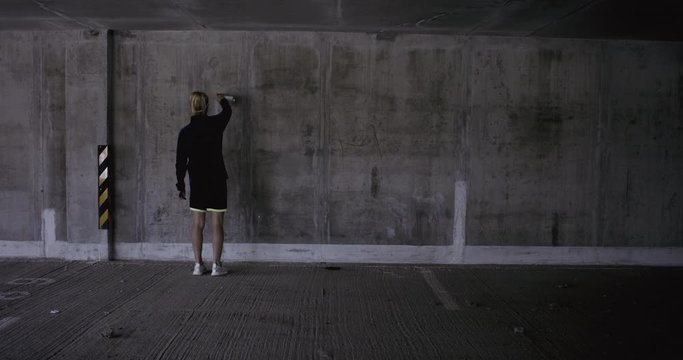 Teenager girl soccer player using a spray paint to draw goals and targets on a wall in empty abandoned covered parking. 4K UHD 60 FPS RAW graded footage