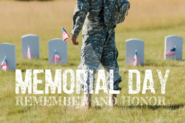 cropped view of military man holding american flag near headstones in graveyard with memorial day,...