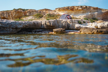 Gray tent on a rocky seashore. View from the water