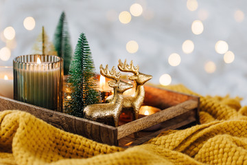 Burning candles and christmas decorations on wooden tray with warm plaid. Winter cozy style. Hygge...