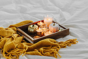 Burning candles pumpkin decoration on wooden tray with warm plaid in bed. Autumn style. Hygge...