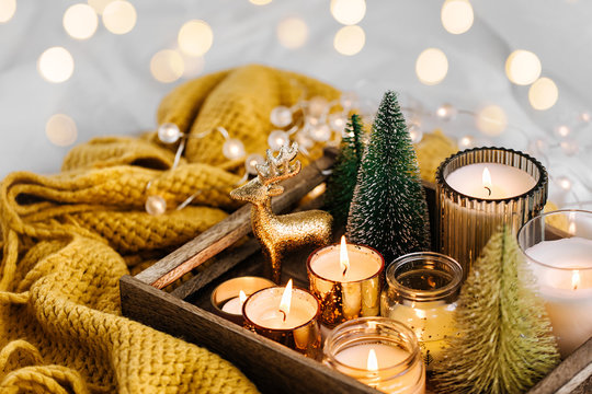 Burning candles and christmas decorations on wooden tray with warm plaid. Winter cozy style. Hygge concept.