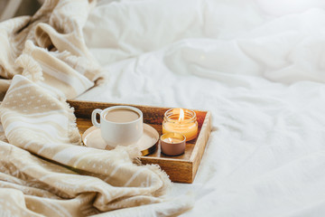 Fototapeta na wymiar Tray of coffee and candles with warm plaid on white bedding . Breakfast in bed. Scandinavian style. Flat lay, top view