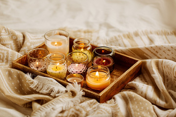Burning candles on wooden tray with warm plaid in bed.  Scandinavian style. Hygge concept.