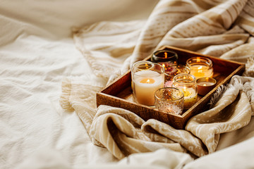 Burning candles on wooden tray with warm plaid in bed.  Scandinavian style. Hygge concept.