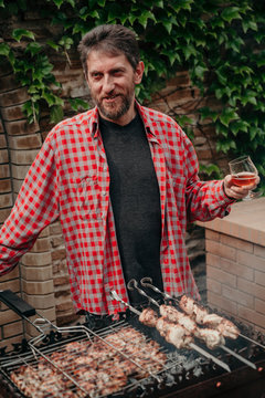 Man With Beard Drinks Beer In Front Of Smoky Barbecue