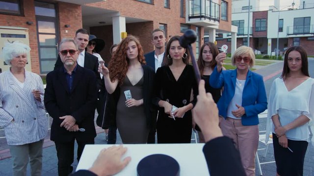 Ongoing auction. Rich and confident people making ids showing paddles with numbers. Close-up auctioneer calling out bids and leading a bulic sale event.