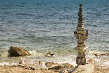 Fototapeta na wymiar Cairn of pebbles on the black sea. Zen stack of stones with turquoise background.