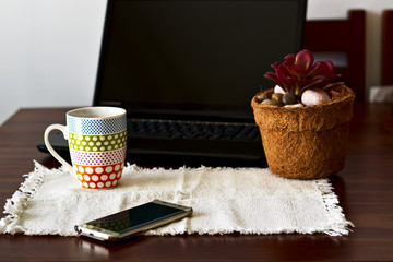 Computer next to a cup of coffee, a plant and a cell phone.