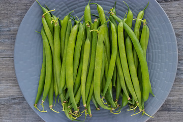 Green asparagus beans on a gray plate on a gray wooden background. The concept of healthy eating, vegetarianism and a raw food diet.
