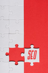 top view of incomplete jigsaw near white puzzle piece with seo lettering isolated on red
